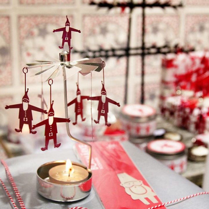 Rotary candle holder creates a cozy atmosphere and perfect as an interior detail. Just light the candle and watch the little metal santa figures rotate. Candle holder is gold-coloured with red details and comes in a box. 1 tealight candle is included. Height approx.17cm.